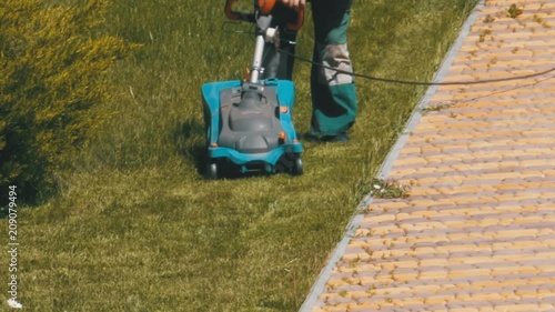 Man with an Portable Electric Lawnmower Mows the Green Grass on the Lawn in the Park. Gardening worker mower mows the lawn. photo