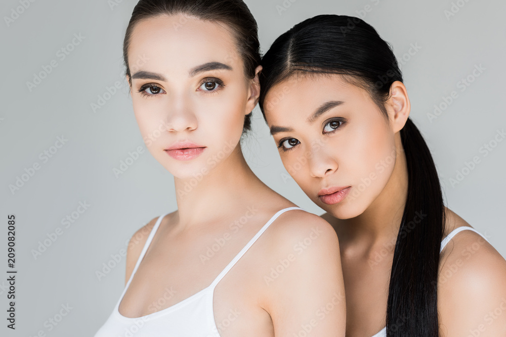 portrait of attractive asian and caucasian young women looking at camera isolated on gray background portrait of attractive asian and caucasian young women looking at camera isolated on gray background