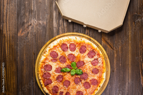 Pizza pepperoni with mozzarella cheese, salami and arugula with box on wooden background