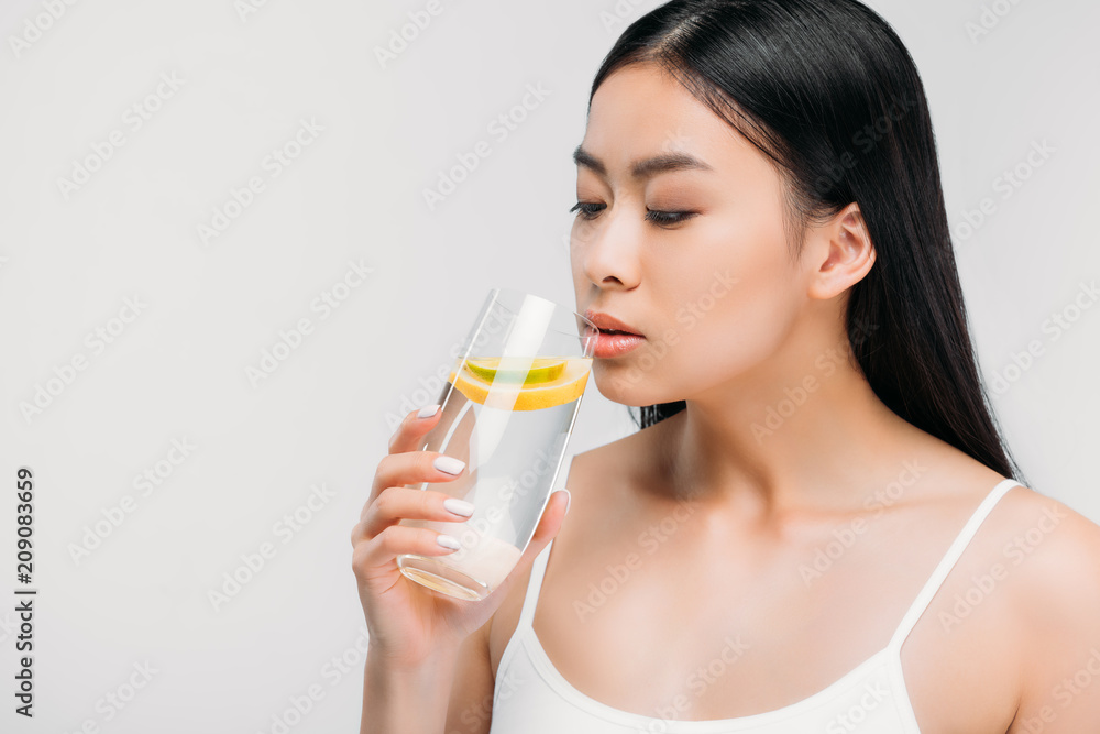 charming asian girl drinking pure water with lemon, isolated on grey charming asian girl drinking pure water with lemon, isolated on grey