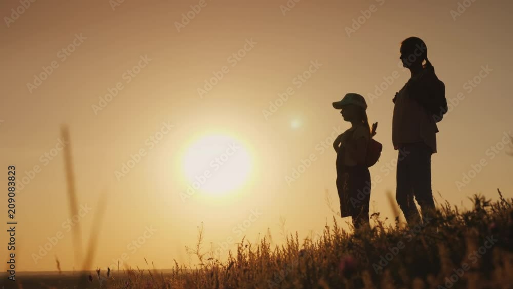 Mom and daughter are admiring the sunrise. They stand with backpacks behind their backs in a picturesque place. Traveling with children concept Mom and daughter are admiring the sunrise. They stand with backpacks behind their backs in a picturesque place. Traveling with children concept