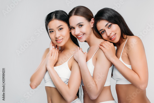 multicultural smiling women posing in white bra, isolated on grey