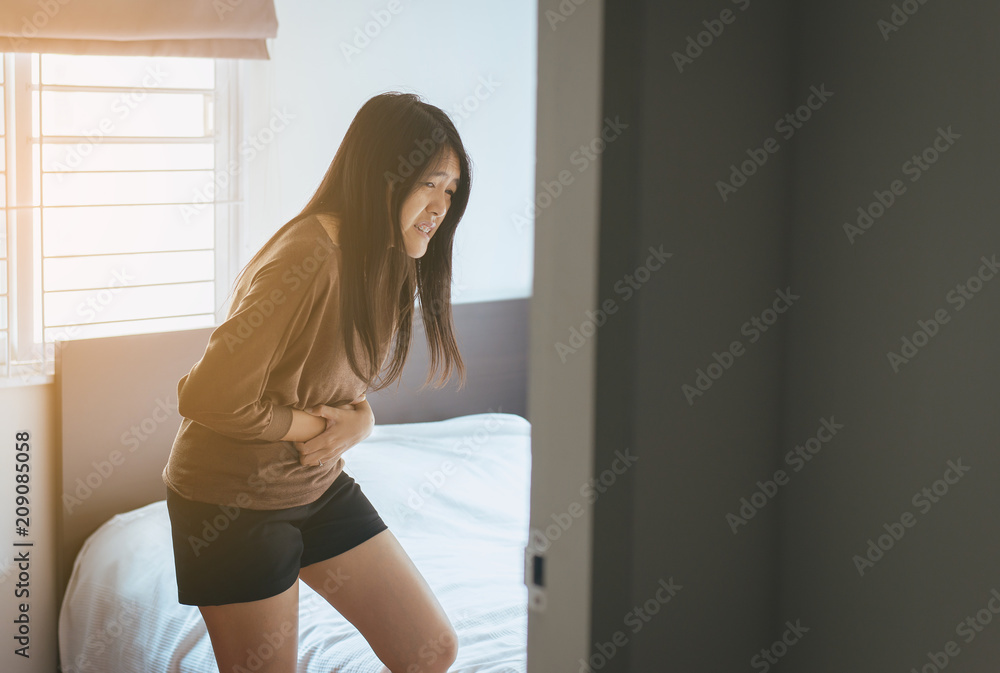 Asian woman having painful stomachache and gastritis in bedroom after wake up,Hands touching her stomach Asian woman having painful stomachache and gastritis in bedroom after wake up,Hands touching her stomach