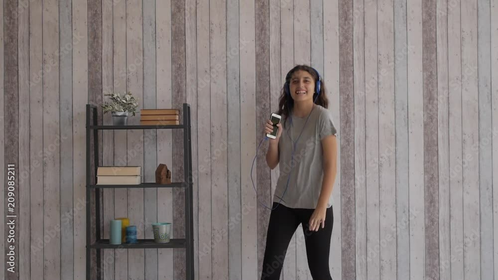 Young girl is dancing in the room with bookcase and phone style.