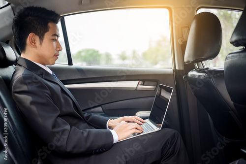 Handsome Young businessman using laptop and sitting in back seat of car. © snowing12