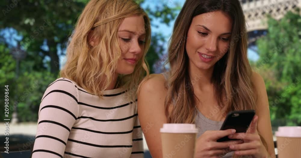 Close up of pretty brunette woman showing blonde friend smart phone by Eiffel Tower in Paris, France, Close view of two friends sharing smartphone in front famous French monument, 4k Close up of pretty brunette woman showing blonde friend smart phone by Eiffel Tower in Paris, France, Close view of two friends sharing smartphone in front famous French monument, 4k