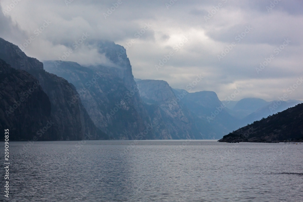 View of a norwegian Lysefjord surrounded by high mountains on a cloudy rainy day, view from ship, Rogaland, Norway