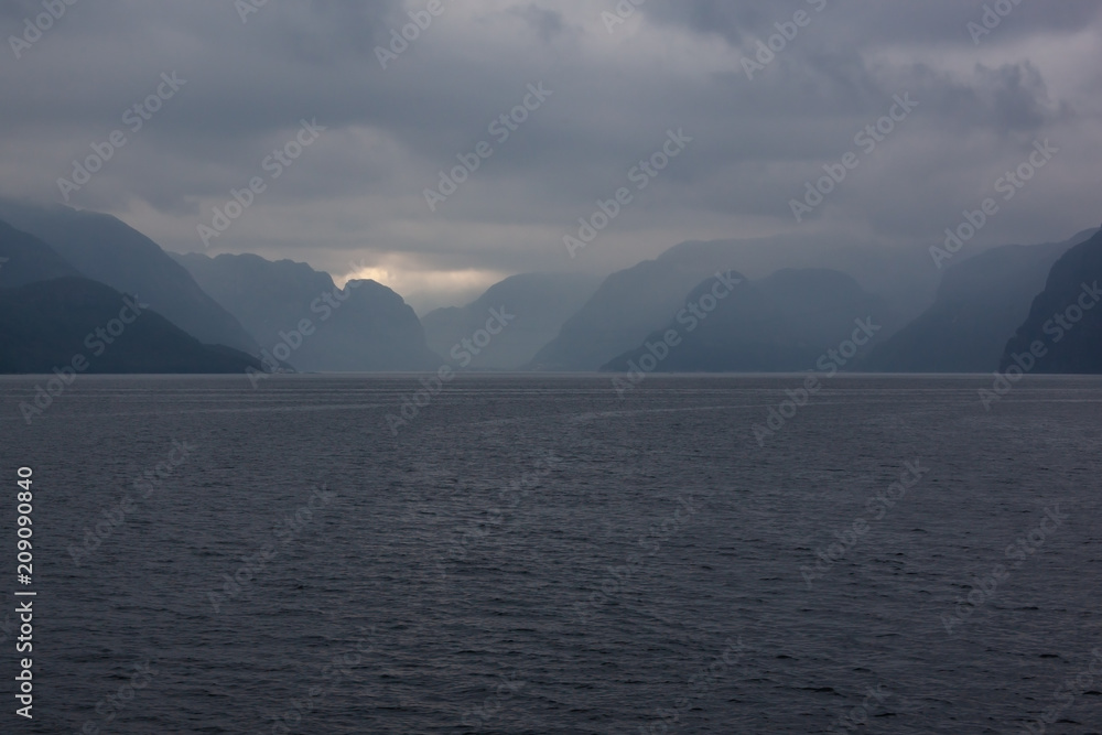 View of a norwegian Lysefjord surrounded by high mountains on a cloudy rainy day, view from ship, Rogaland, Norway View of a norwegian Lysefjord surrounded by high mountains on a cloudy rainy day, view from ship, Rogaland, Norway