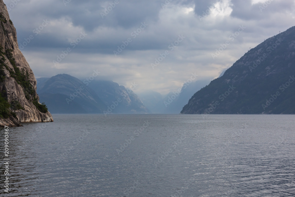 View of a norwegian Lysefjord surrounded by high mountains on a cloudy rainy day, view from ship, Rogaland, Norway