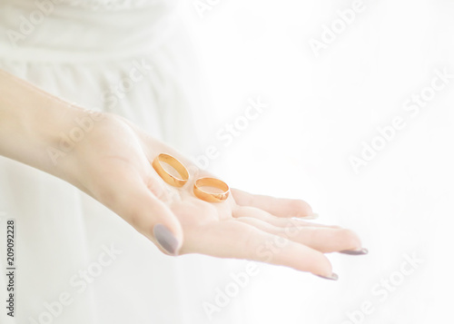 Close-up young bride's hand holding two golden wedding rings on open palm. Wedding tradition and symbol. White background with soft light