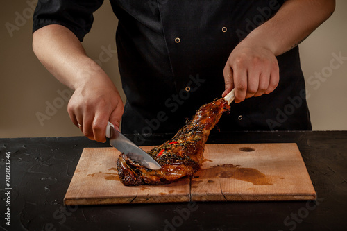 Chef is cutting roasted leg lamb on wooden board on table