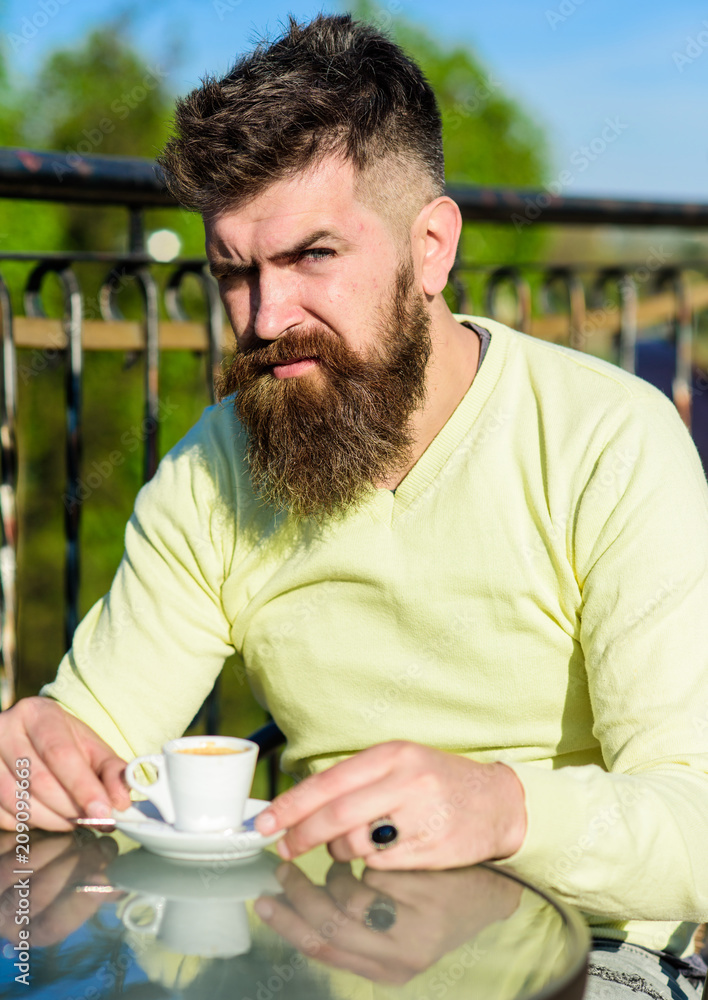 Bearded man with espresso cup, drinks coffee. Coffee break concept. Man with beard and mustache on strict face, fence of terrace on background, defocused. Man with long beard looks strict and serious. Bearded man with espresso cup, drinks coffee. Coffee break concept. Man with beard and mustache on strict face, fence of terrace on background, defocused. Man with long beard looks strict and serious.