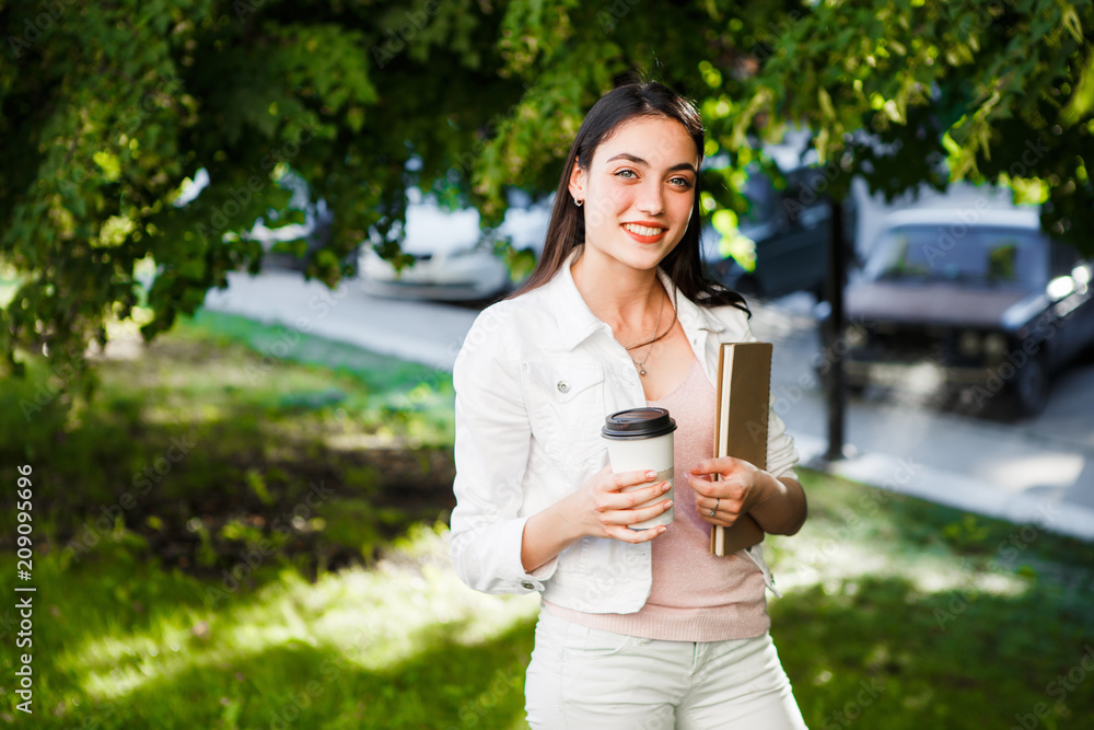 Beautiful girl with coffee and a notebook on a green summer street. Beautiful girl with coffee and a notebook on a green summer street.