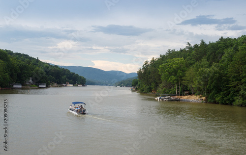 A beautiful summer landscape with a lake in the background of the mountains. People sail on a boat on the lake. Lake Lure, NC, USA © Liudmila