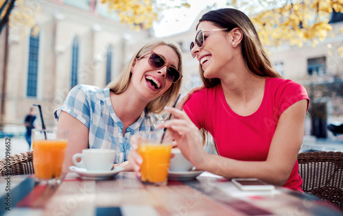 Friends meeting in a cafe. Young women drinking coffee and enjoying in conversation. Consumerism, lifestyle concept