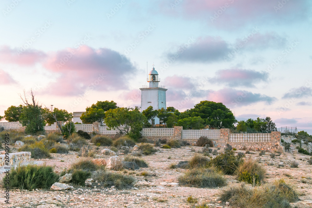 Lighthouse in the coastal town of Santa Pola, Valencia, Costa Blanca in Spain. Beautiful, pink sky, in the foreground plants and stones. Lighthouse in the coastal town of Santa Pola, Valencia, Costa Blanca in Spain. Beautiful, pink sky, in the foreground plants and stones.