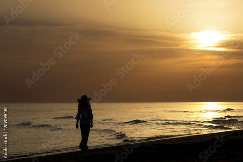 A young woman walking on the beach along the seaside at sunset