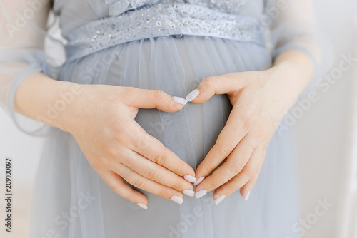 belly of a pregnant girl close-up. Gray dress. A gentle embrace and stroking the pregnant belly.