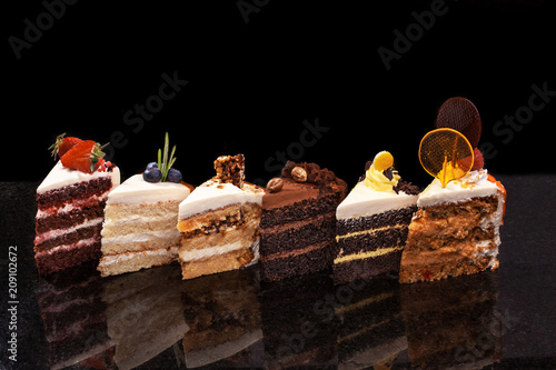 Assorted large pieces of different cakes: chocolate, raspberries, strawberries, nuts, blueberries. Pieces of cakes on a black table. photo