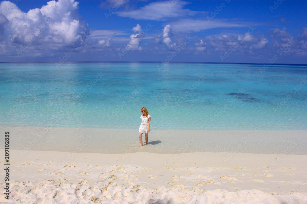 Young pretty woman in white dress walking on a white sand beach in Maldives under clear blue sky Young pretty woman in white dress walking on a white sand beach in Maldives under clear blue sky