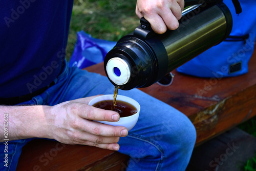 Men's hands pour tea. Hands holding a mug and a thermos. A man pours tea from a thermos into a Cup. Outdoor recreation.