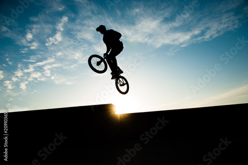 silhouette of extreme cyclist jumping high on blue sky background sunset