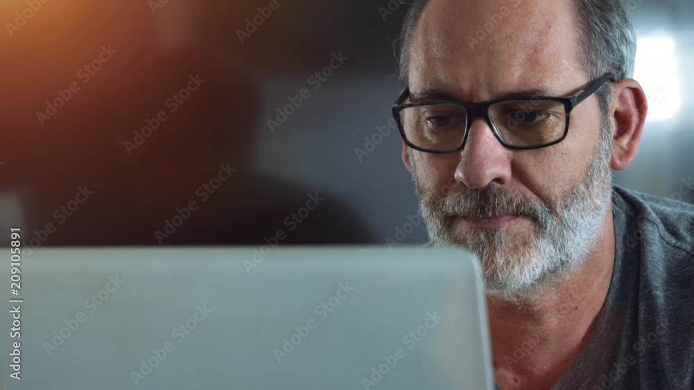 Casual smart Businessman works with Laptop computer in his Office - smooth tracking shot with nice reflections in background
