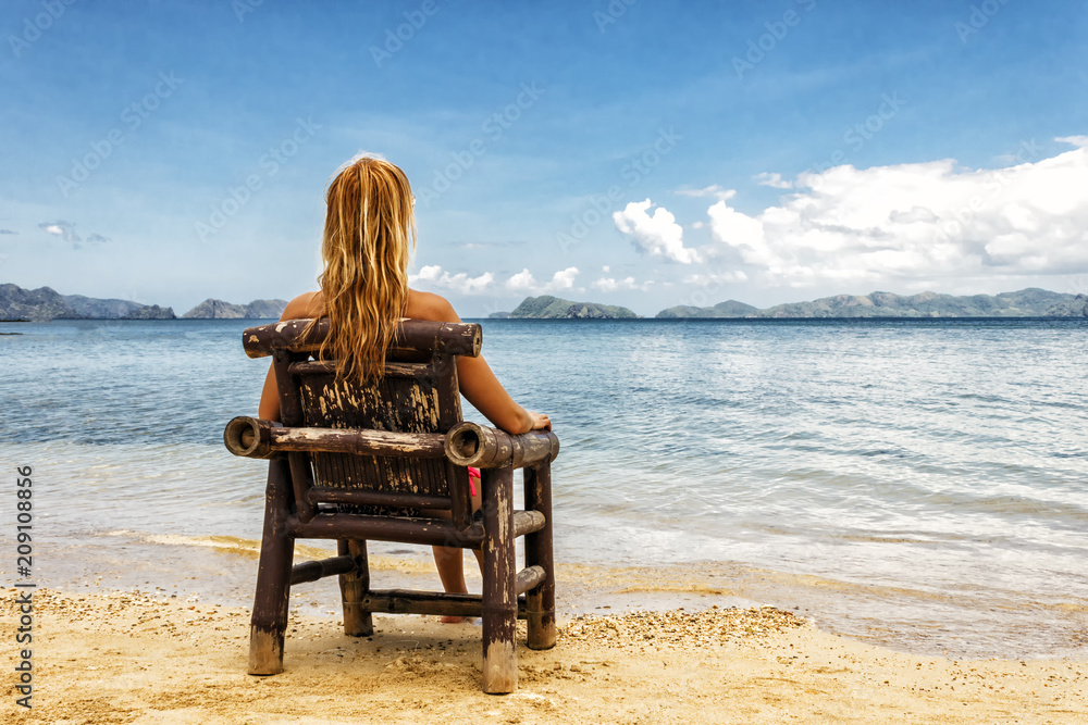 A girl sitting on a bamboo chair on the beach on a blue sea and sky background. place for text.