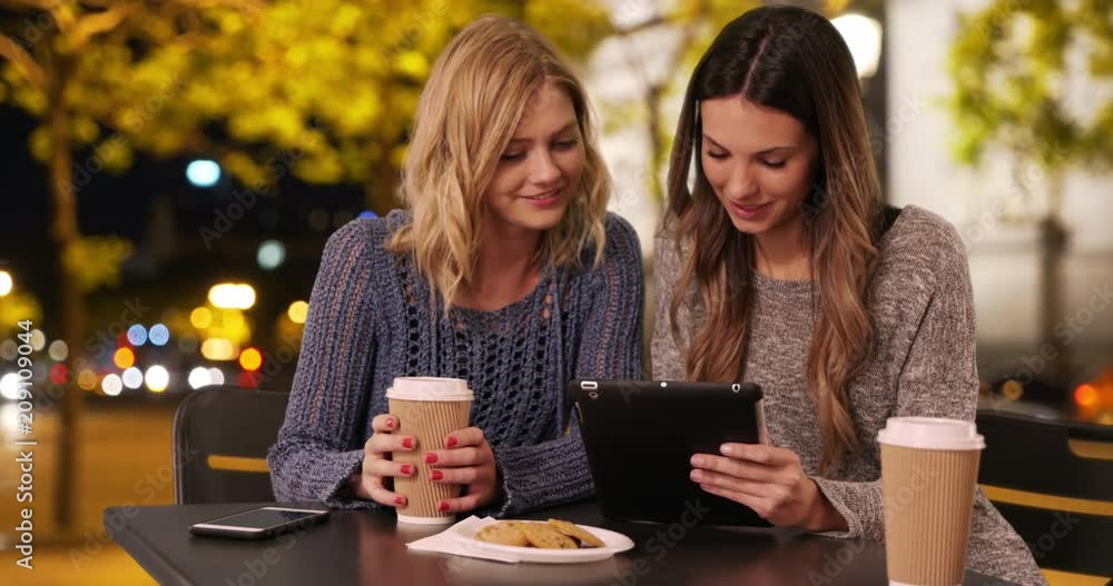 Lovely couple of girls sharing tablet computer near the Arch of Triumph Champs Elysees, Paris, France, Two attractive young women using portable tablet while drinking at table in Parisian plaza, 4k