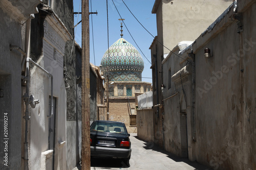wąska uliczka w arabskim kraju z domami i ozdobną kopułą meczetu w tle