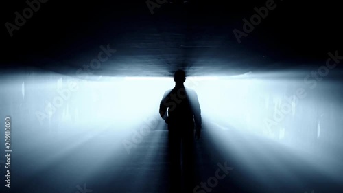 Silhouette of person walking in tunnel to the bright light.