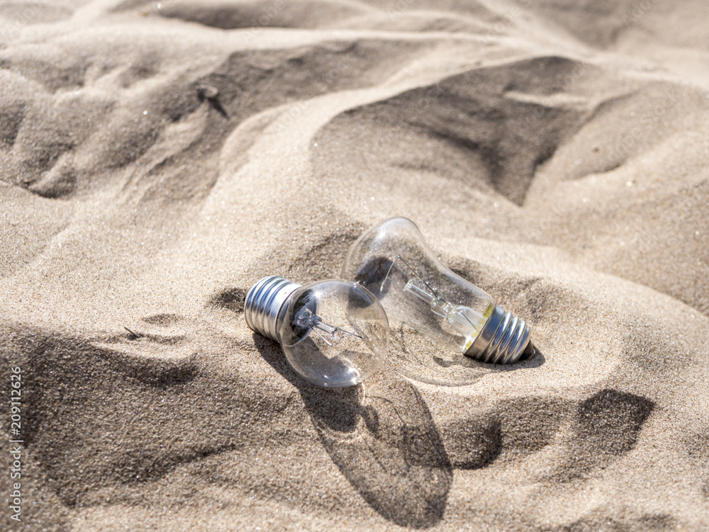 two incandescent lamps dropped on the sand on summer sunny day two incandescent lamps dropped on the sand on summer sunny day