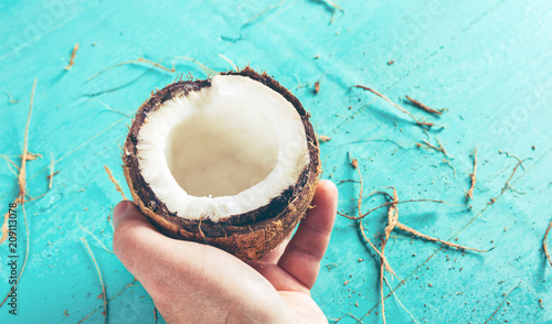 Half of a chopped coconut in a hand on a blue background with a peel