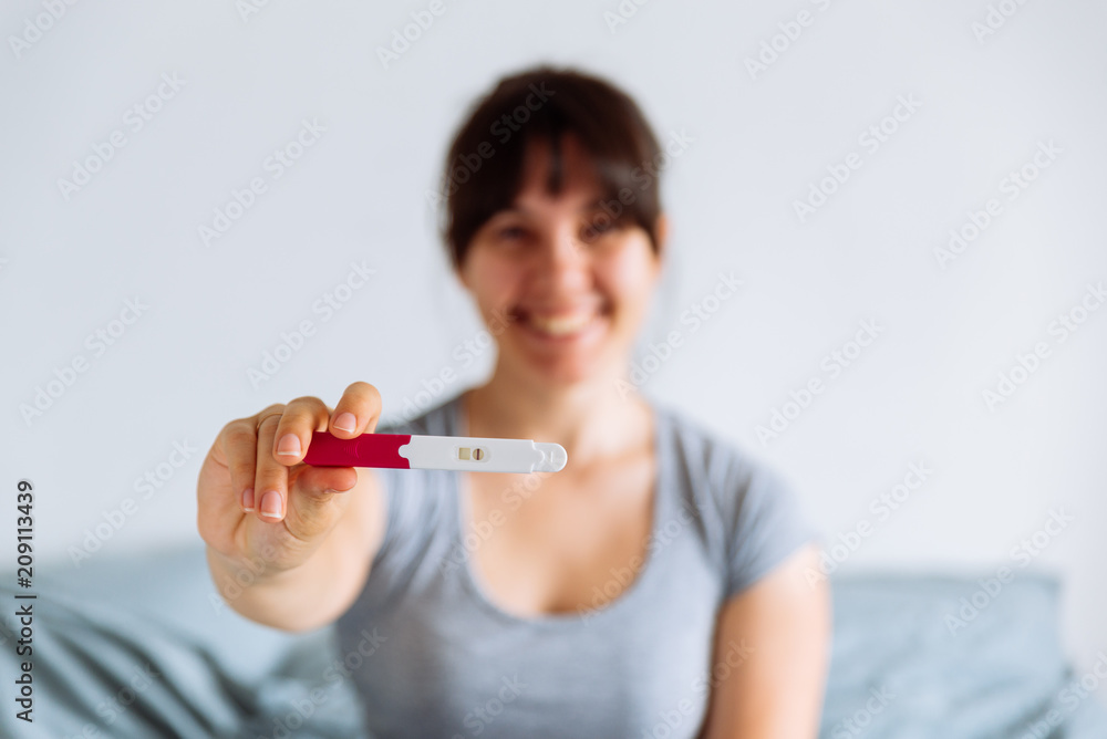 young happy woman sitting on bed looking on positive pregnancy test young happy woman sitting on bed looking on positive pregnancy test