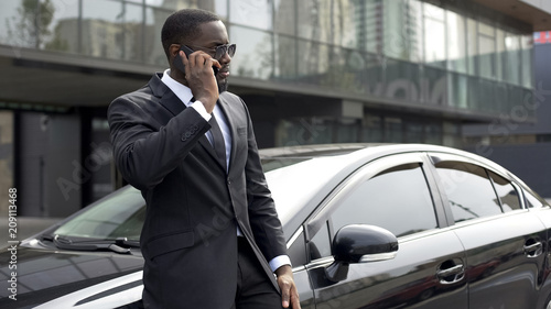 Successful man in expensive suit communicating on phone, standing near his car