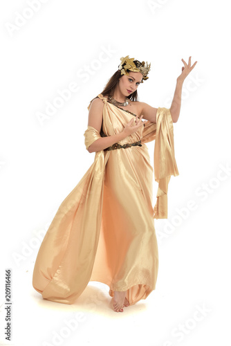 full length portrait of brunette woman wearing long golden grecian gown, standing pose. isolated on white studio background.