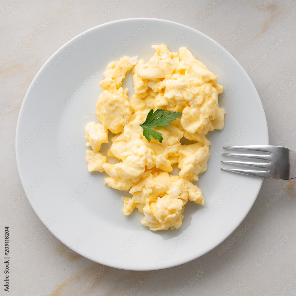 white plate with pan-fried scrambled eggs on white light background with tomatoes. Omelette, top view