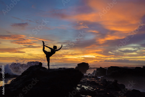 silhouette of a girl practicing yoga at sunset on a background of waves