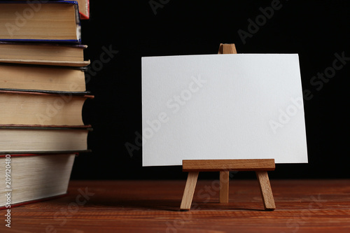 A stack of books on a table, on a black background. A small easel, a white blank, a blank, a mock-up. © Plutmaverick