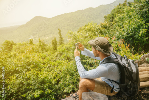 man with a beard hiker in a T-shirt and hat with a backpack and an action camera takes pictures of the landscape on the fide and photos. Travel and technology.