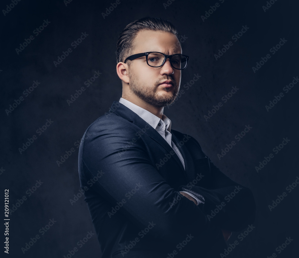 Handsome stylish businessman with serious face in an elegant formal suit standing with crossed arms. Isolated on a dark background.