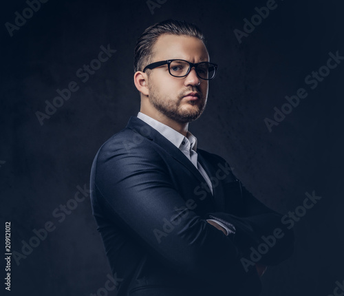 Handsome stylish businessman with serious face in an elegant formal suit standing with crossed arms. Isolated on a dark background.