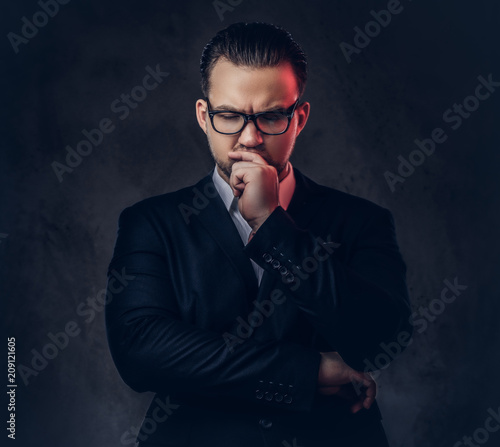 Close-up portrait of a thoughtful stylish businessman with serious face in an elegant formal suit and glasses on a dark background.