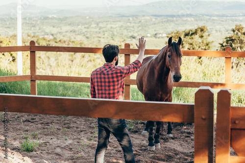 Young farmer taming horse in corral