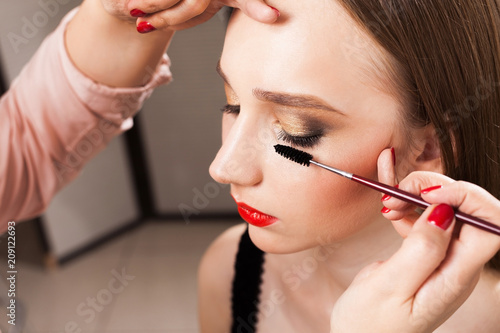 close up photo of make up artist carefully applying a mascara on lashes of a beautiful model with flawless makeup in a beauty studio photo