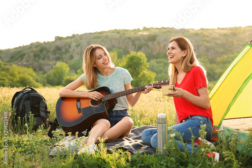 Young women resting with hot drink and guitar near camping tent in wilderness © New Africa