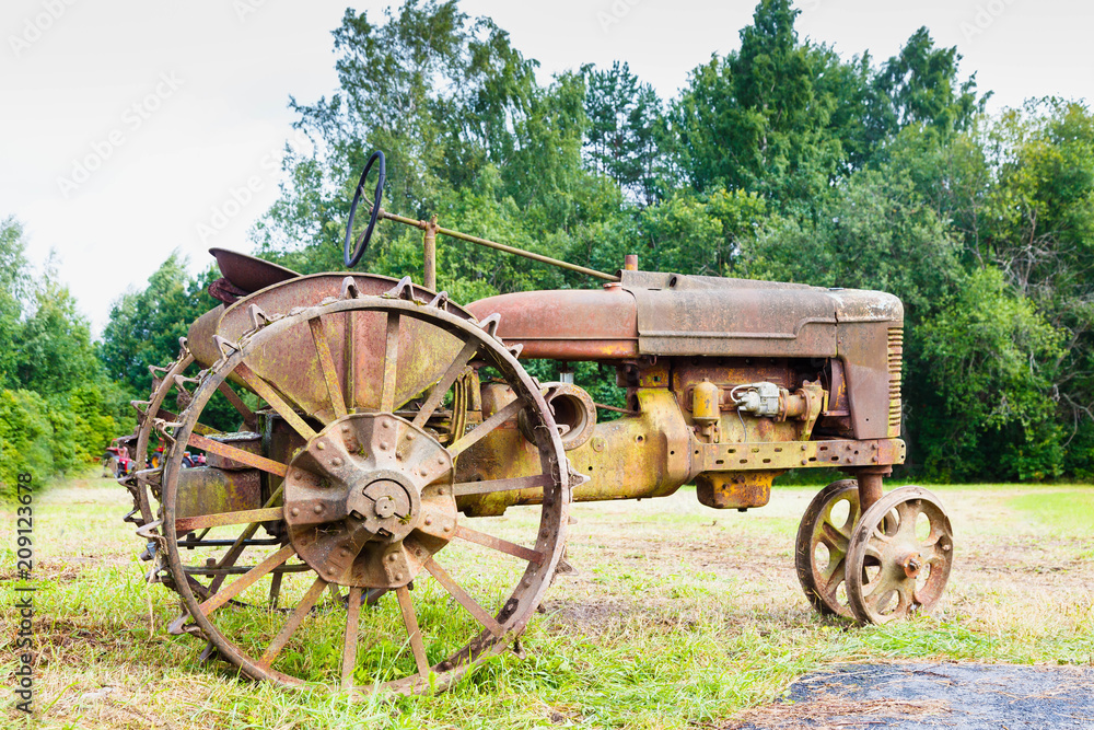 Very old rusted tractor sitting in a green field under a bright blue sky in the summer time