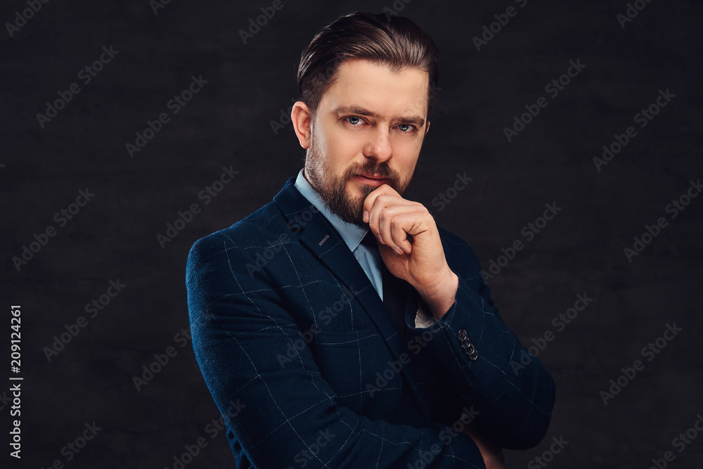 Pensive middle-aged man with beard and hairstyle dressed in an elegant blue suit. Isolated on a textured dark background in a studio. 