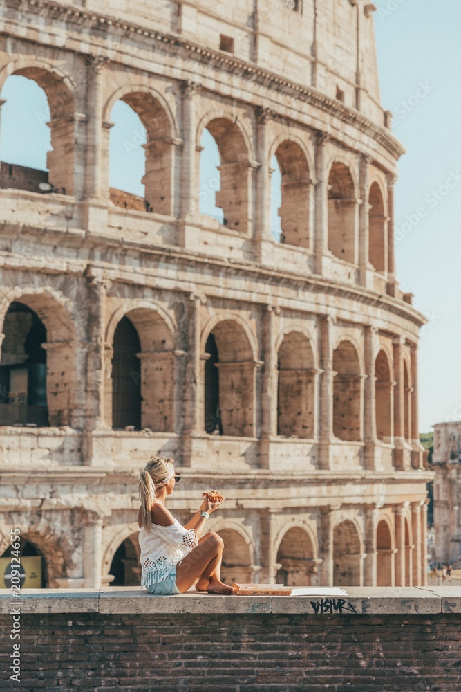 Girl eating a pizza front of the colosseum