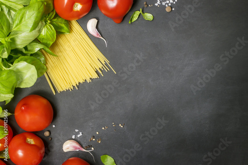 Food frame. Pasta ingredients. Tomatoes, spaghetti pasta, garlic, basil and spices on dark backdrop, copy space, top view, horizontal oriented